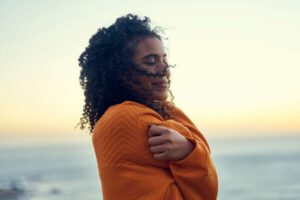 woman smiling and hugging herself with a sunset in the background